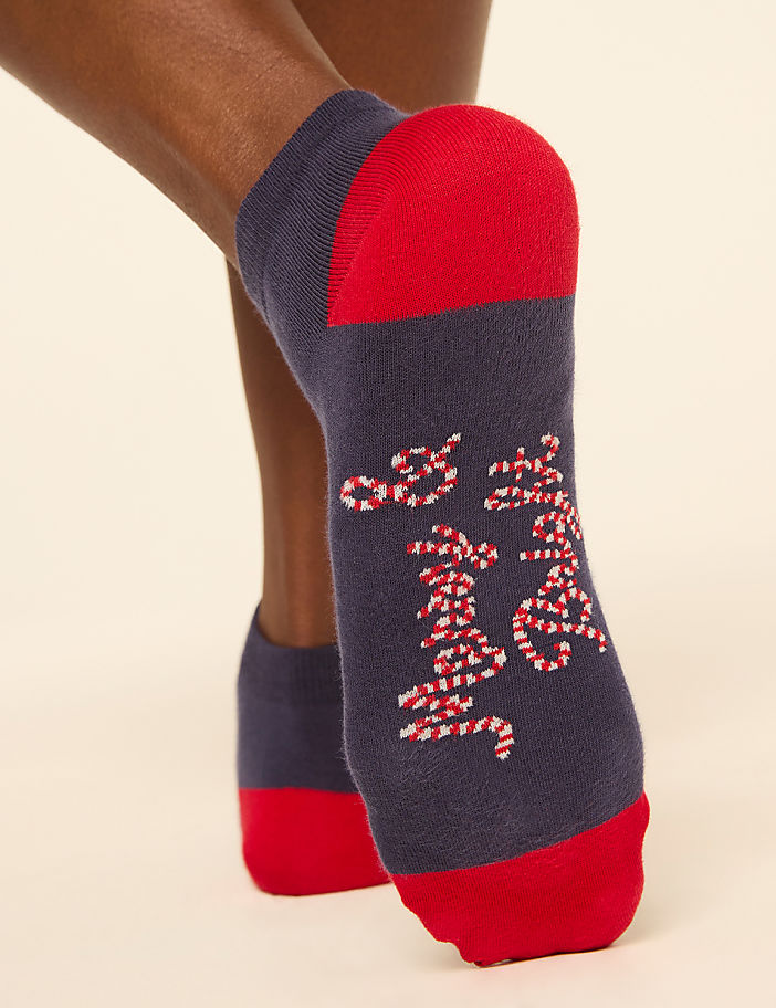A close-up of a person's feet wearing navy blue socks with red toes and heels, adorned with a candy cane pattern, against a plain, light-colored background.