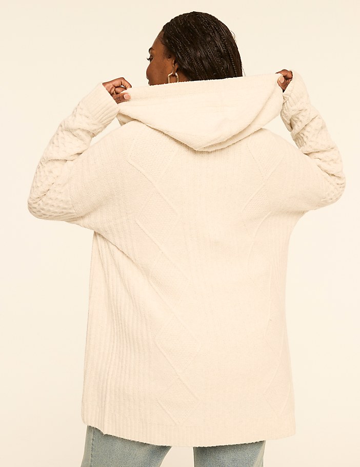 A woman in a cream-colored hooded sweater is shown from the back against a plain, light-colored background.