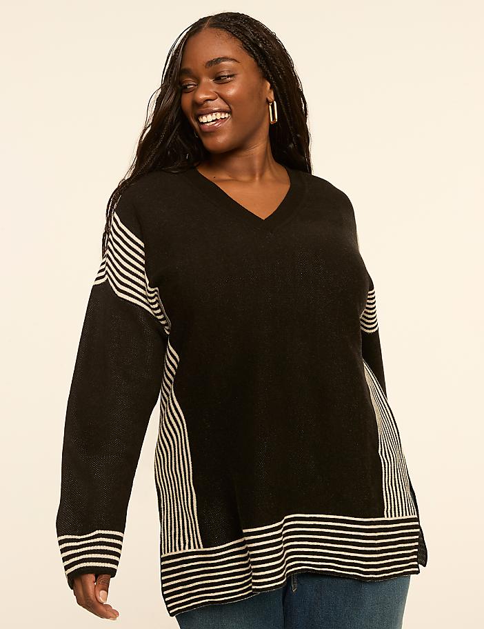 A smiling woman in a black and white striped sweater stands against a plain, light-colored background.