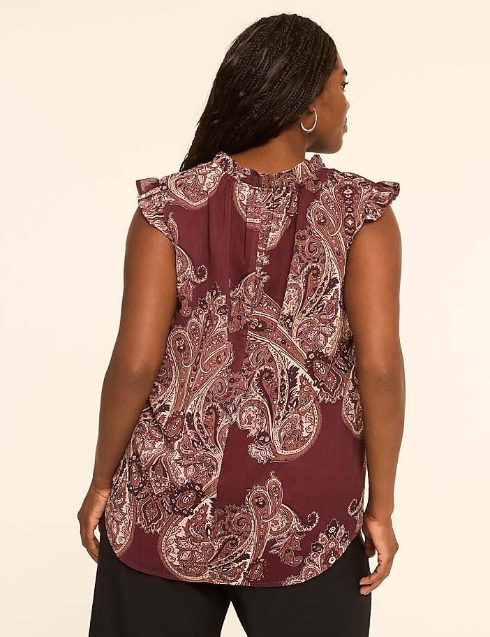 A woman in a paisley-patterned blouse stands against a plain, light-colored background.