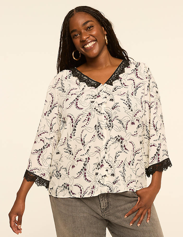 A smiling woman in a floral blouse stands against a plain, light-colored background.