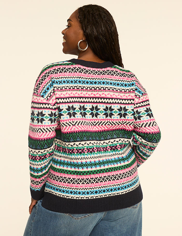 A woman in a colorful, patterned sweater stands against a plain, light-colored background.