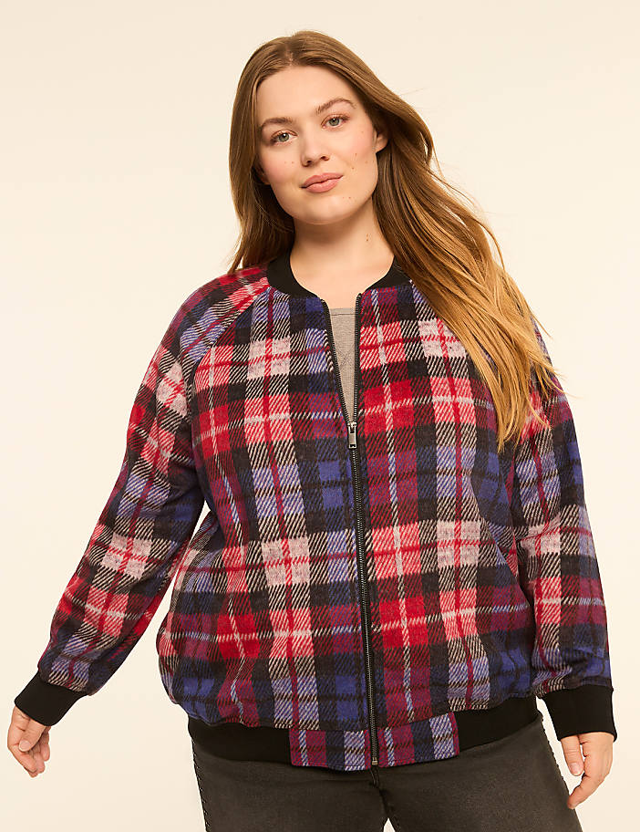 A woman in a plaid bomber jacket stands against a plain, light-colored background.