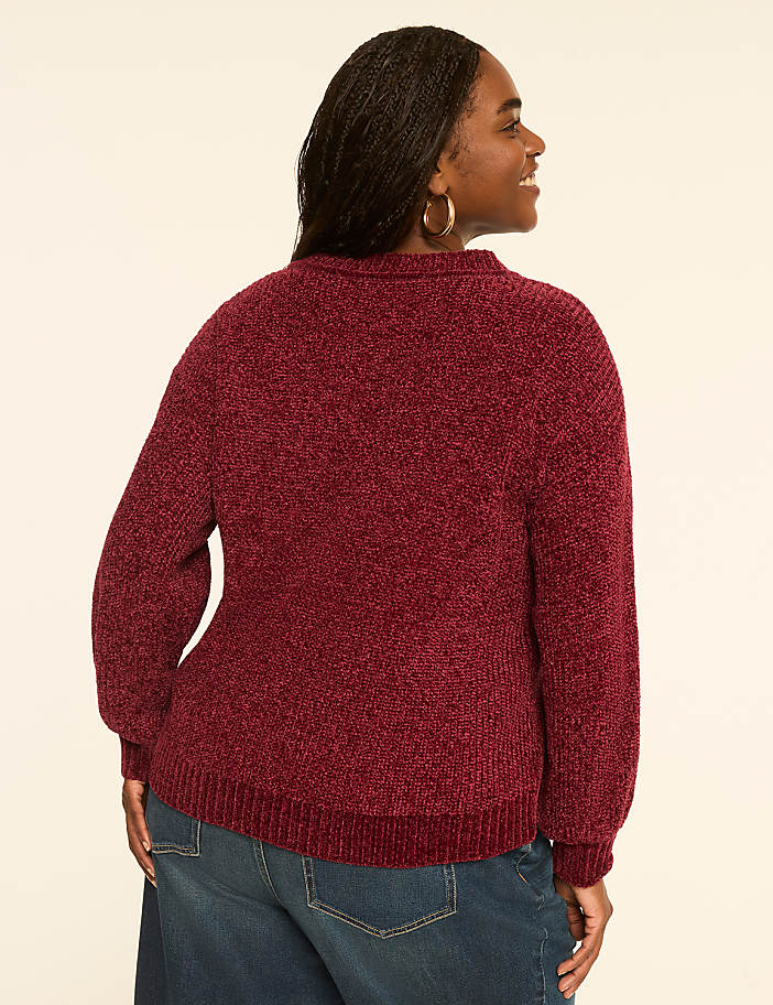 A woman in a burgundy chenille sweater and blue jeans stands against a plain, light-colored background.