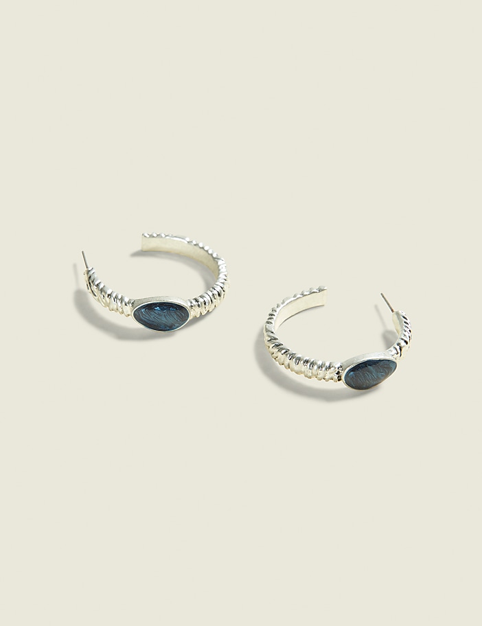 A pair of silver hoop earrings with dark oval stones are displayed against a soft, light brown background.