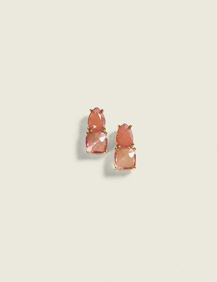 Two gold earrings with stacked square and teardrop-shaped pink gemstones rest on a plain, light beige background.