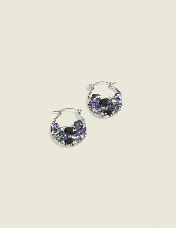 A pair of silver hoop earrings filled with purple, black, and clear stones rest on a pale yellow background.