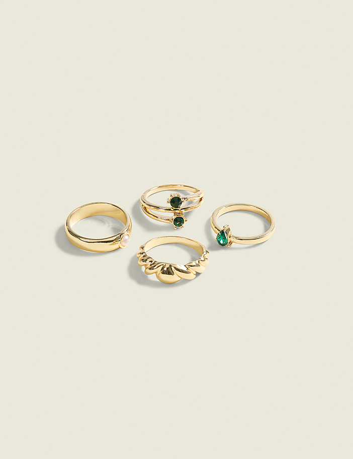 Four gold rings, two with green stones, are arranged on a plain, light-colored background.