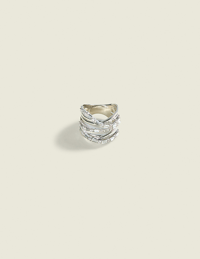 A detailed silver ring with multiple bands and sparkling stones rests on a plain, light-colored background.