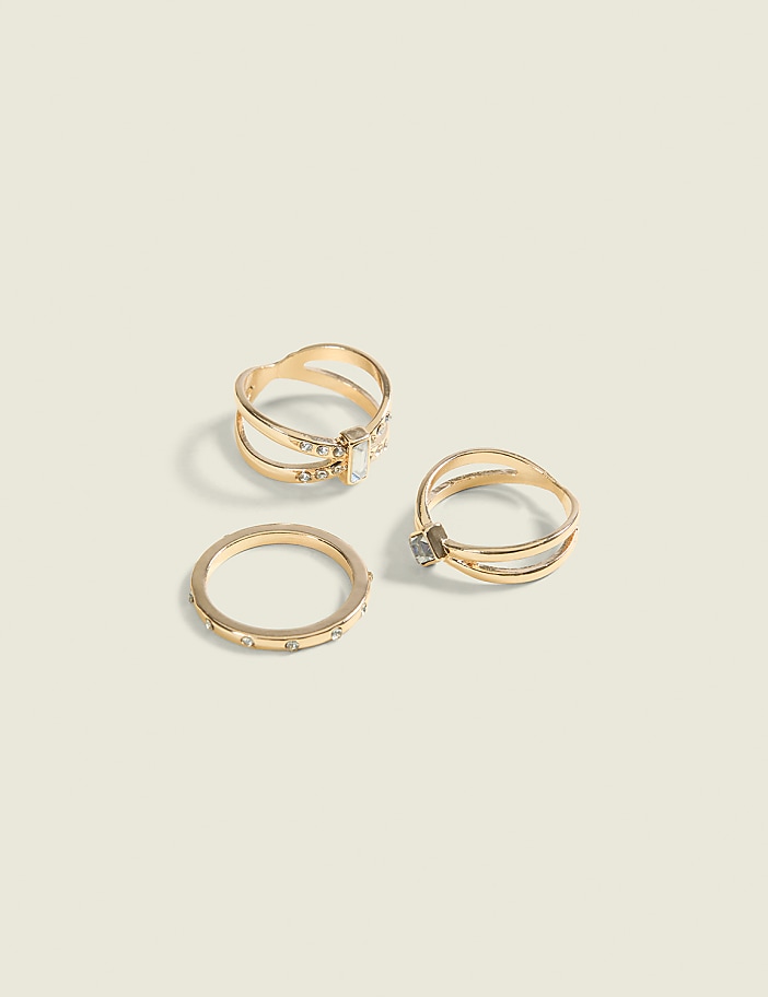 Three gold rings with small stones are arranged on a plain, light-colored surface.