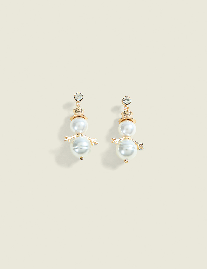 A pair of snowman-shaped pearl earrings with crystal accents dangle against a plain, light beige background.
