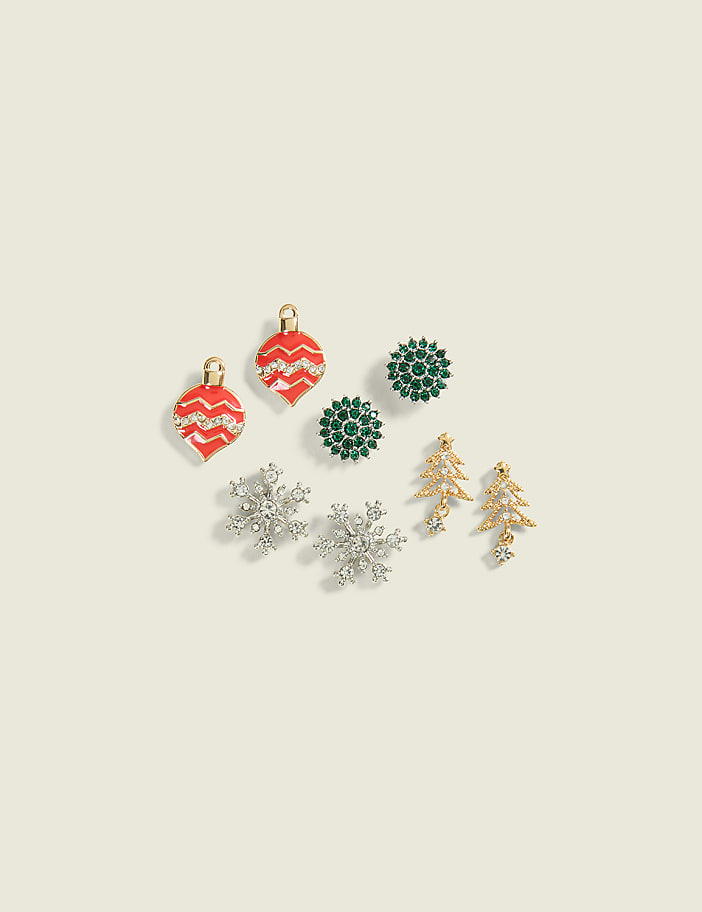 A collection of festive Christmas-themed earrings, including ornaments, snowflakes, and trees, are arranged on a pale cream background.