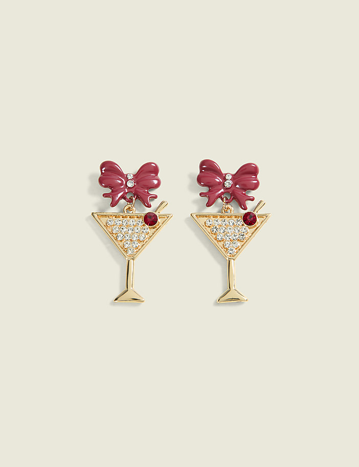 A pair of martini glass-shaped earrings adorned with rhinestones and a red bow sit against a plain, light-colored background.