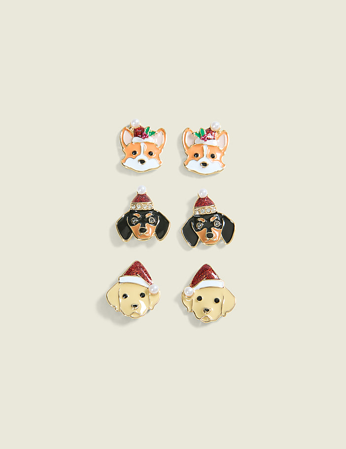 Six festive dog-themed earrings, featuring corgis, dachshunds, and golden retrievers wearing Santa hats, are arranged in two columns against a pale cream background.