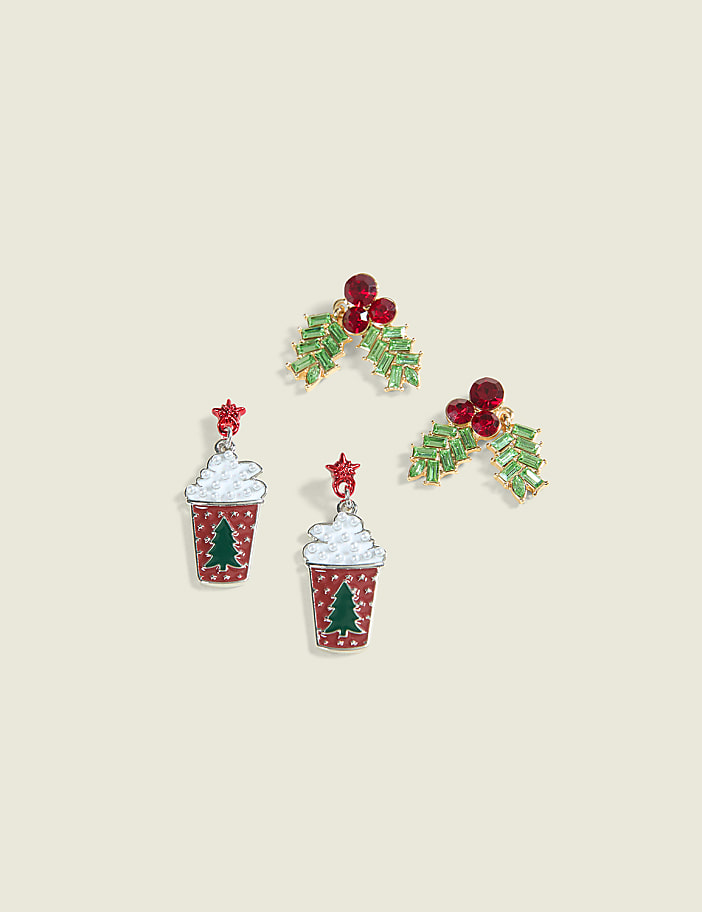 Two pairs of festive Christmas-themed earrings, one with holly and berries and the other resembling a holiday drink, are arranged on a plain, light-colored background.