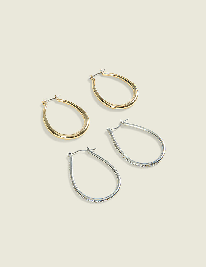 Two pairs of teardrop-shaped hoop earrings, one gold and one silver with rhinestones, rest on a pale, textured background.