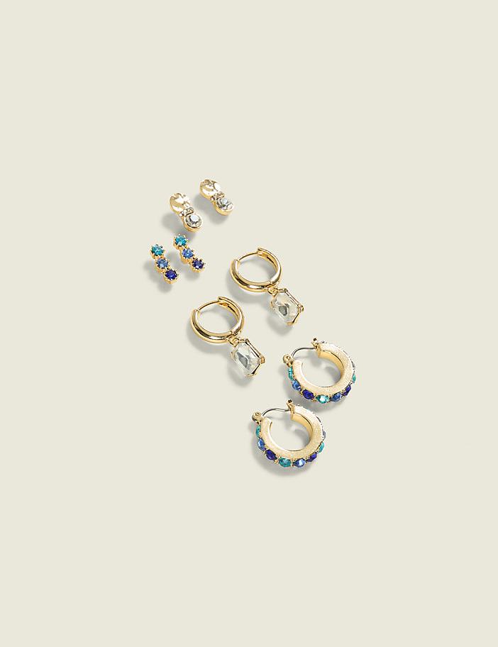 Several pairs of gold earrings with colorful gemstones are arranged on a plain, light-colored background.