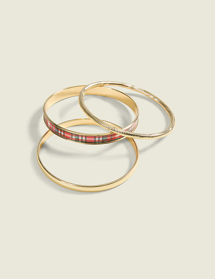 Three gold bangles, one with a red and black plaid pattern, rest on a pale green background.