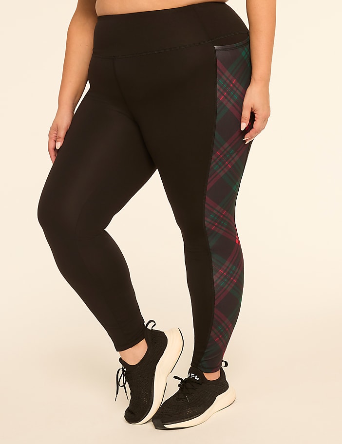 A person wearing black leggings with a plaid side panel and black sneakers stands against a plain, light-colored background.