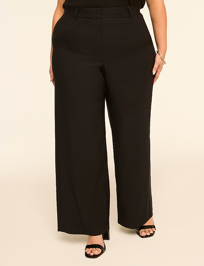 A person wearing black wide-leg pants and black sandals stands against a plain, light-colored background.