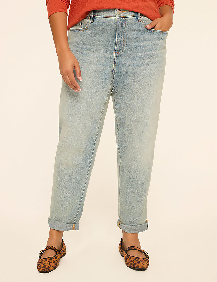 A person wearing light-wash jeans and leopard print flats stands against a plain, light-colored background.