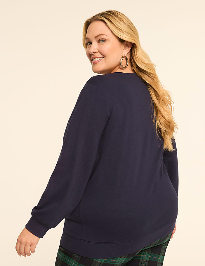 A woman in a navy sweatshirt and plaid pants smiles over her shoulder against a plain, light background.
