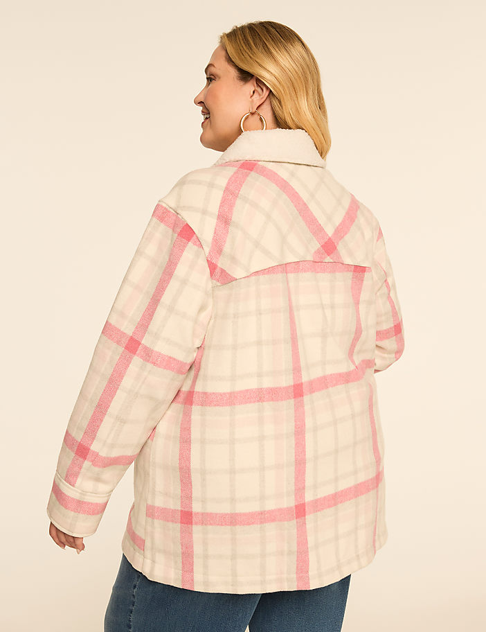 A woman in a cream and pink plaid jacket stands against a plain, light-colored background.