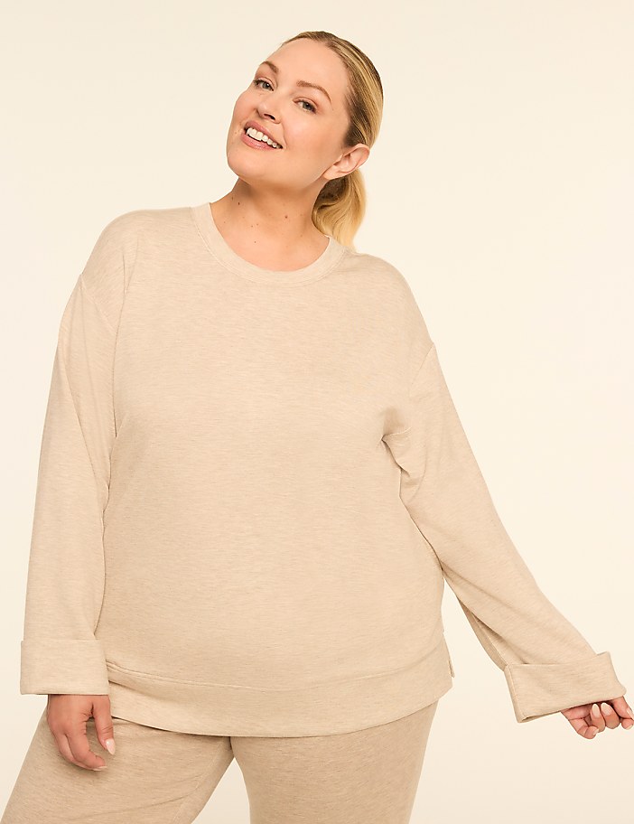 A smiling woman in a beige sweatshirt and pants stands against a plain, light-colored background.