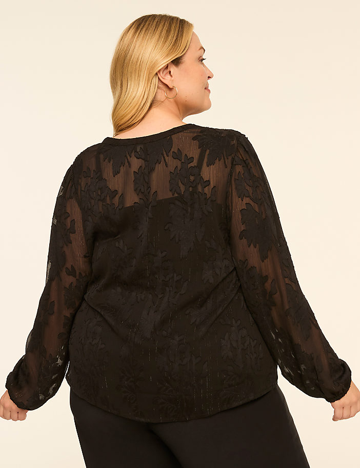 A woman in a black floral lace top stands against a plain, light-colored background.