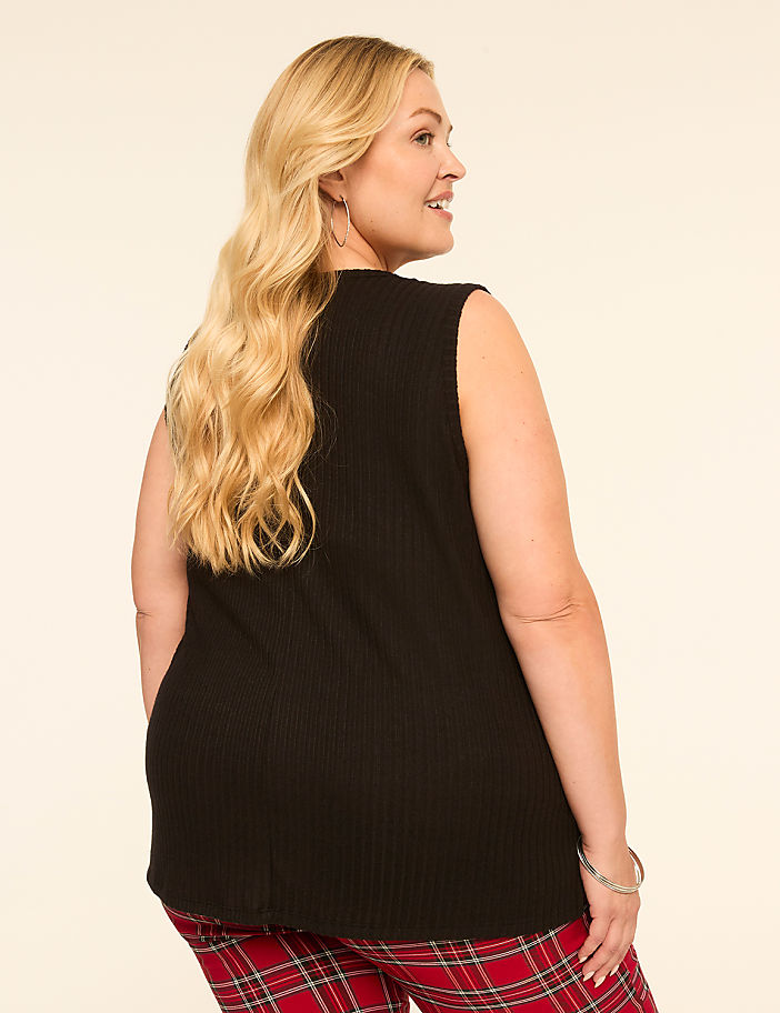A blonde woman in a black sleeveless top and red plaid pants stands against a plain, light-colored background.