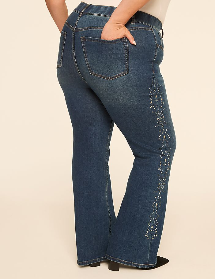 A person's lower body is shown from the side, wearing flared blue jeans with decorative embellishments on the side, against a plain, light-colored background.