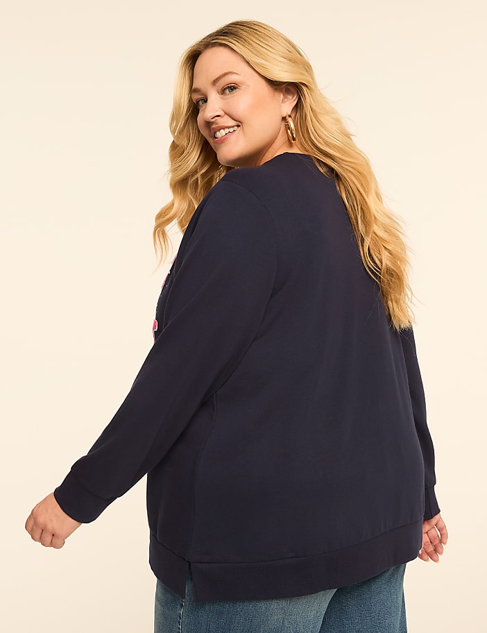 A smiling woman in a navy sweatshirt and jeans poses against a plain, light-colored background.