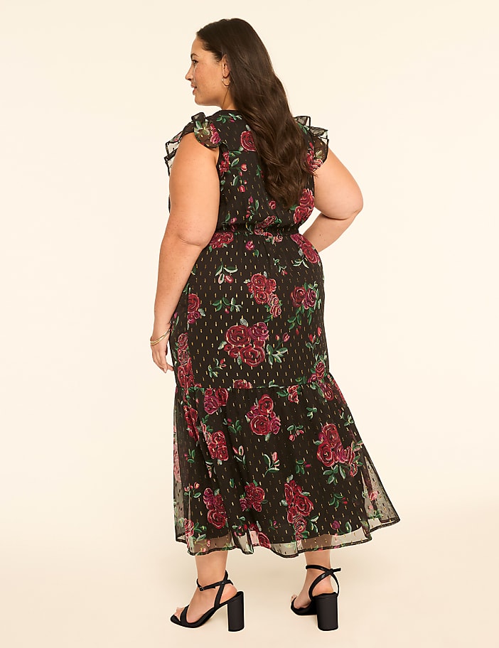 A woman in a floral dress stands against a plain, light-colored background.