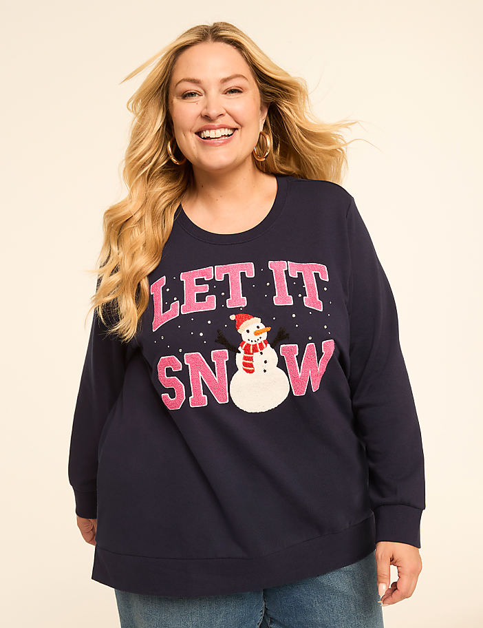 A smiling woman in a navy blue sweatshirt with a snowman graphic and "LET IT SNOW" text stands against a plain, light-colored background.