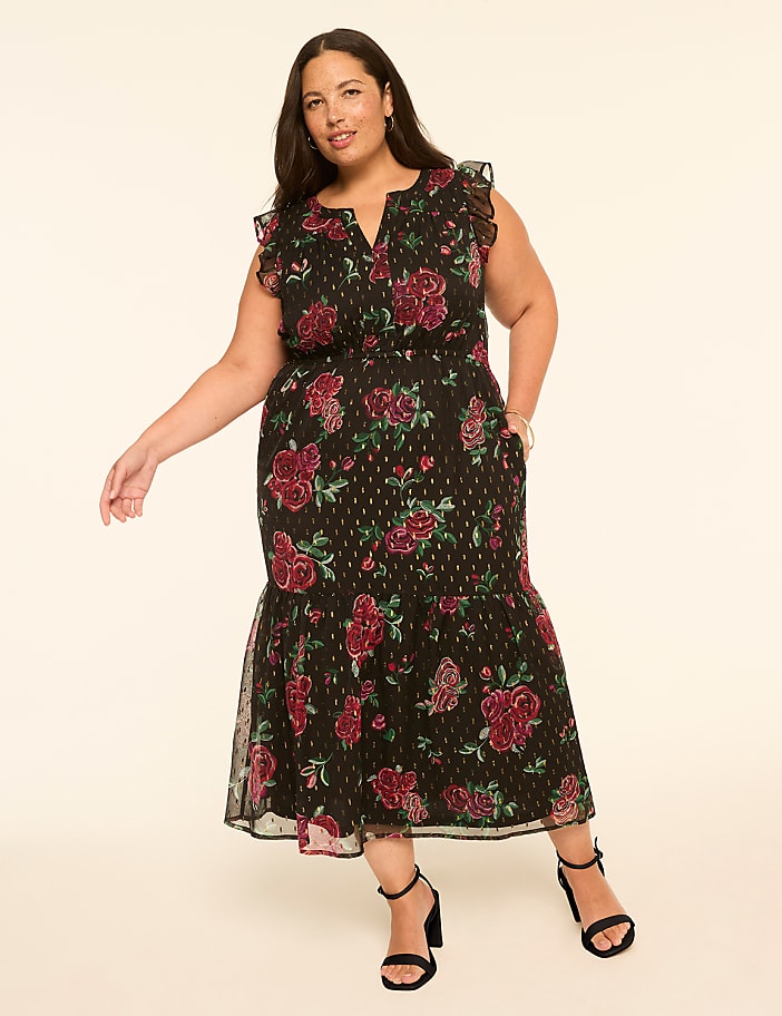 A woman in a floral dress stands against a plain, light-colored background.