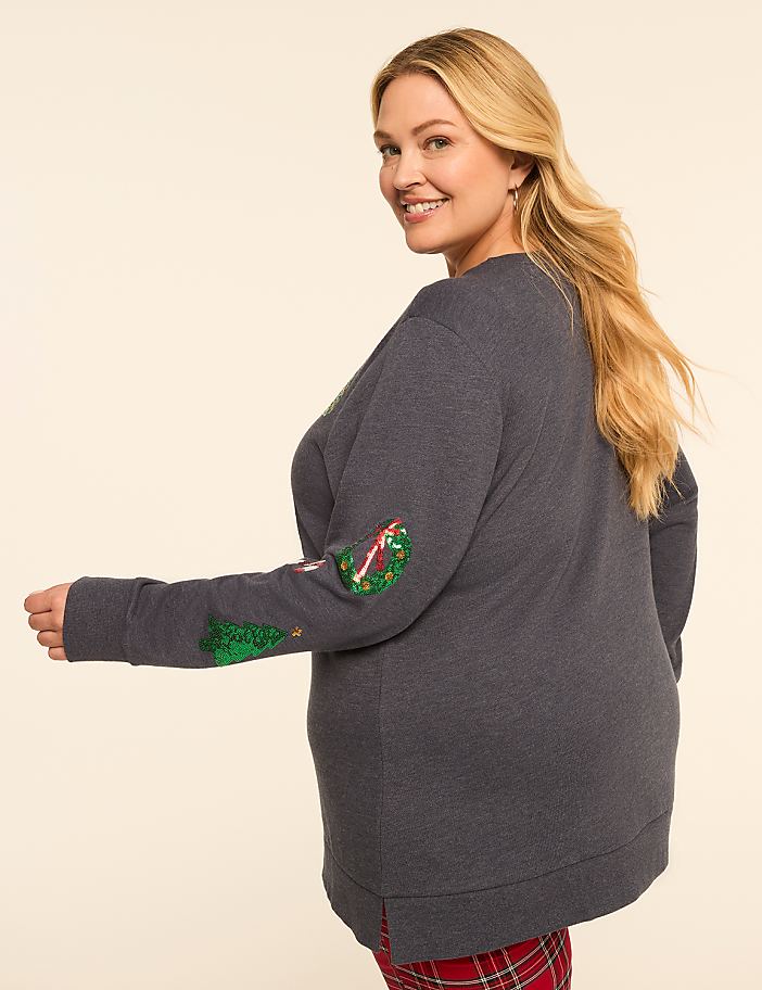 A smiling woman in a grey Christmas-themed sweatshirt and red plaid pajama bottoms poses against a plain, light-colored background.