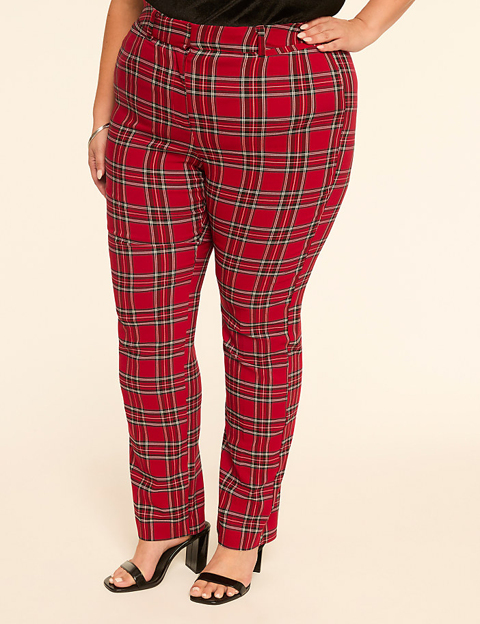 A person stands in front of a plain, light-colored background, wearing red plaid pants and black heels.