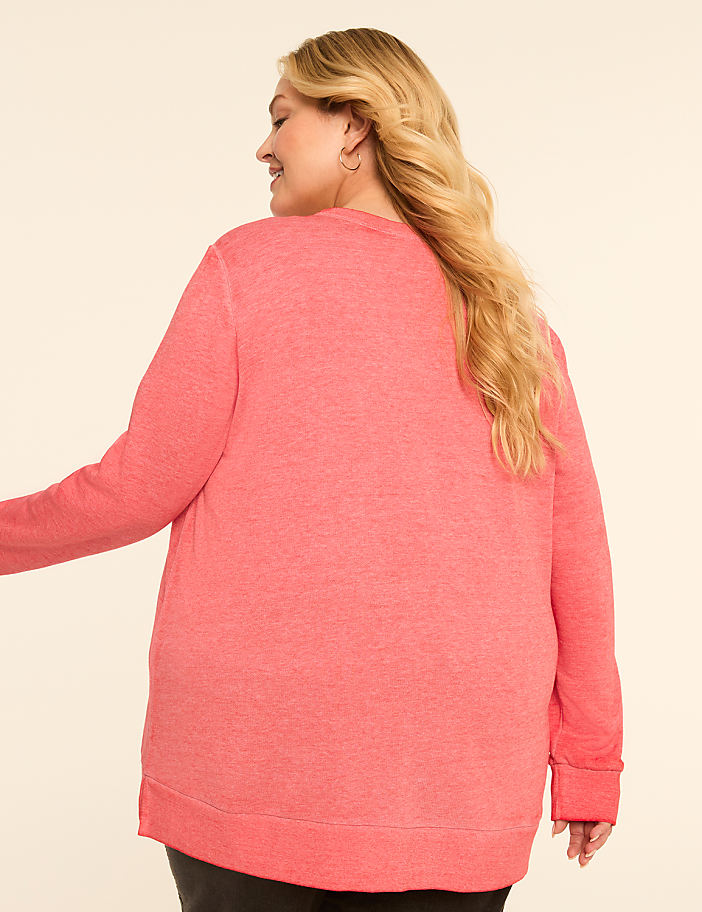 A woman in a coral sweatshirt stands against a plain, light-colored background.
