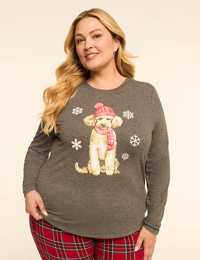 A woman in a grey long-sleeved shirt with a dog graphic and red plaid pants stands against a plain, light background.