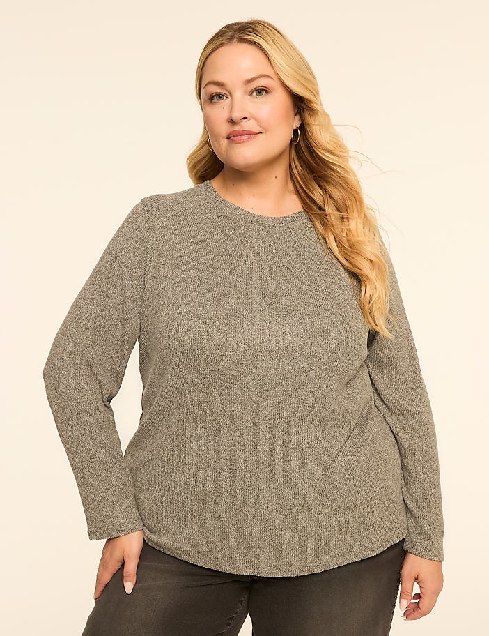 A woman with blonde hair and a gray sweater stands against a plain, light-colored background.