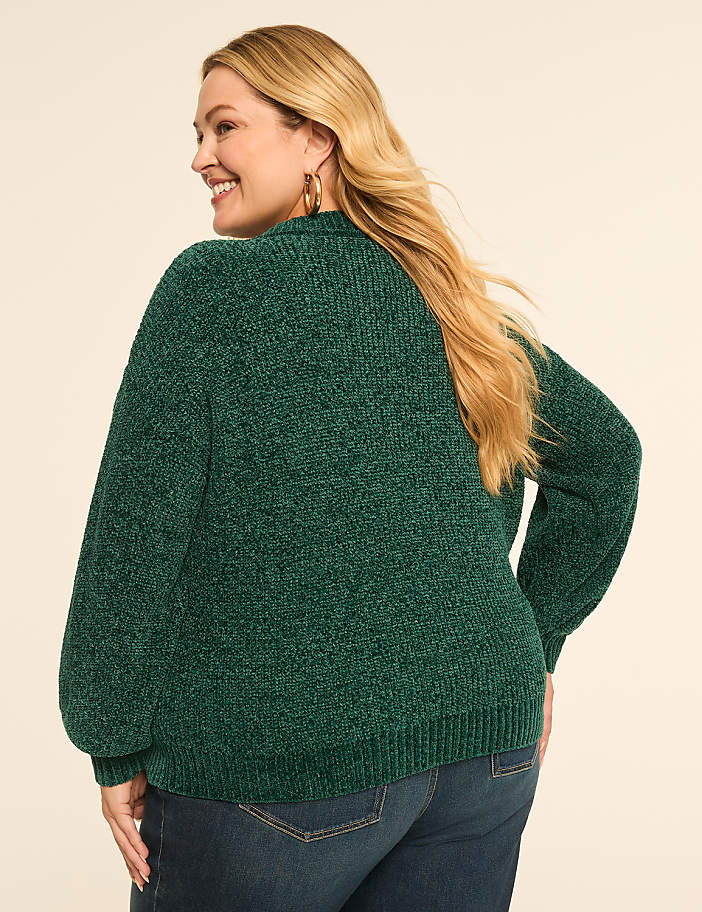 A woman in a green chenille sweater and blue jeans is shown from the back against a plain, light-colored background.