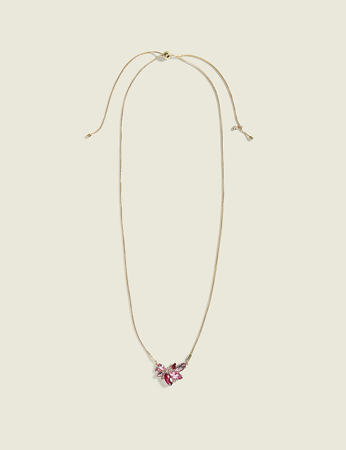 A delicate gold necklace with a cluster of pink and purple crystals rests on a plain, light beige background.