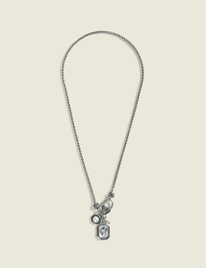 A silver necklace with a rectangular crystal pendant and smaller charms hangs against a plain, light beige background.