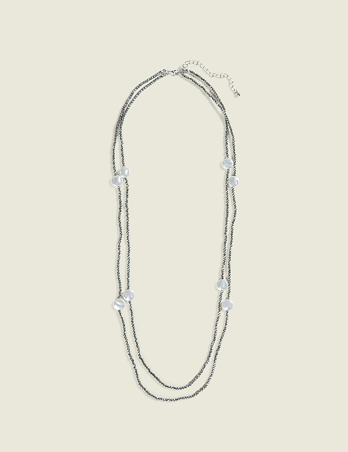 A delicate, double-strand necklace with small gray beads and scattered pearl-like accents lies against a plain, light beige background.