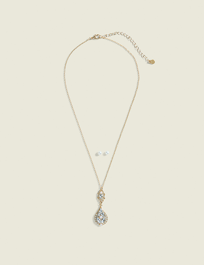 A delicate gold necklace with a teardrop pendant and matching stud earrings rests on a pale cream background.