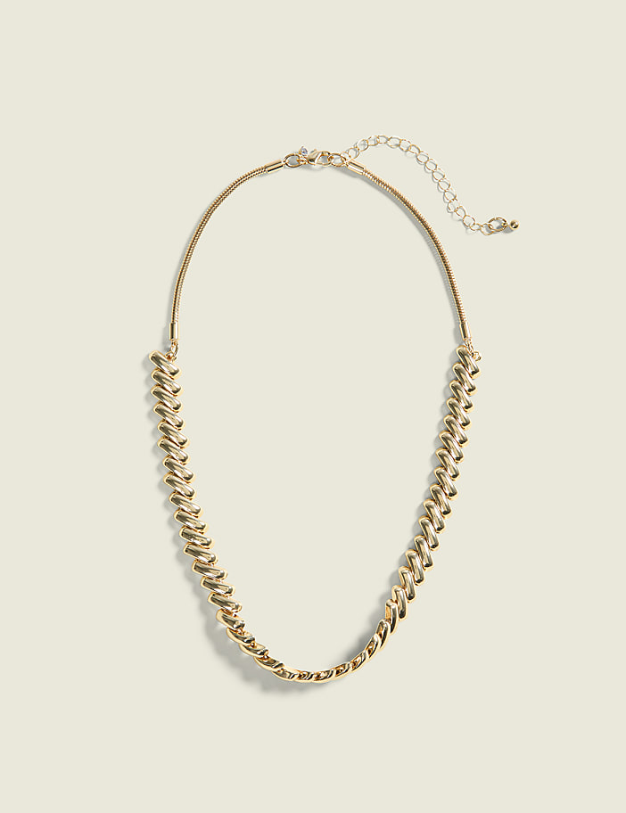 A gold chain necklace with a textured design rests on a pale yellow background.