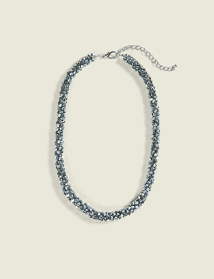 A sparkly, silver beaded necklace with a delicate chain rests on a plain, light beige background.