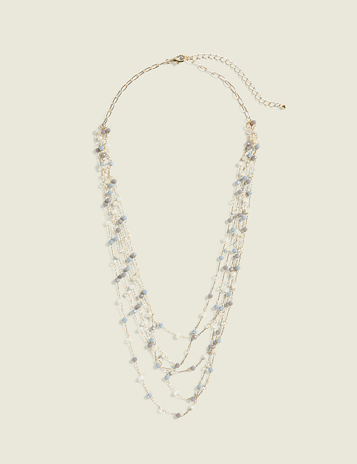 A delicate, multi-strand necklace with small, light-colored beads hangs against a plain, light beige background.