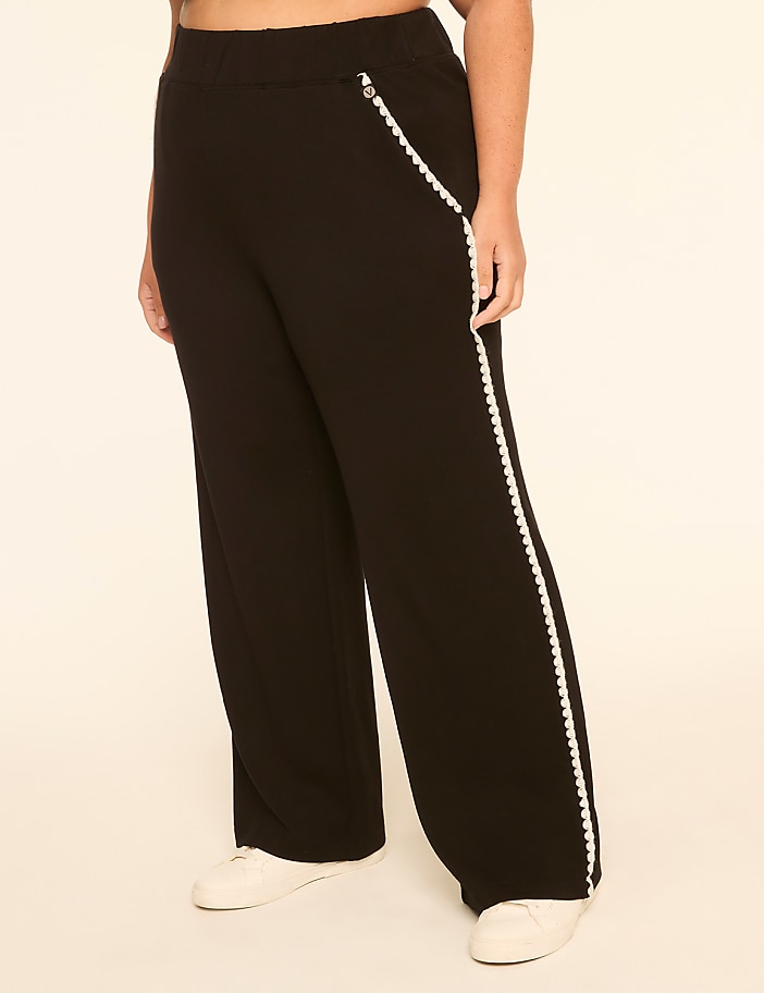 A person stands in black wide-leg pants with white trim, against a plain, light-colored background.