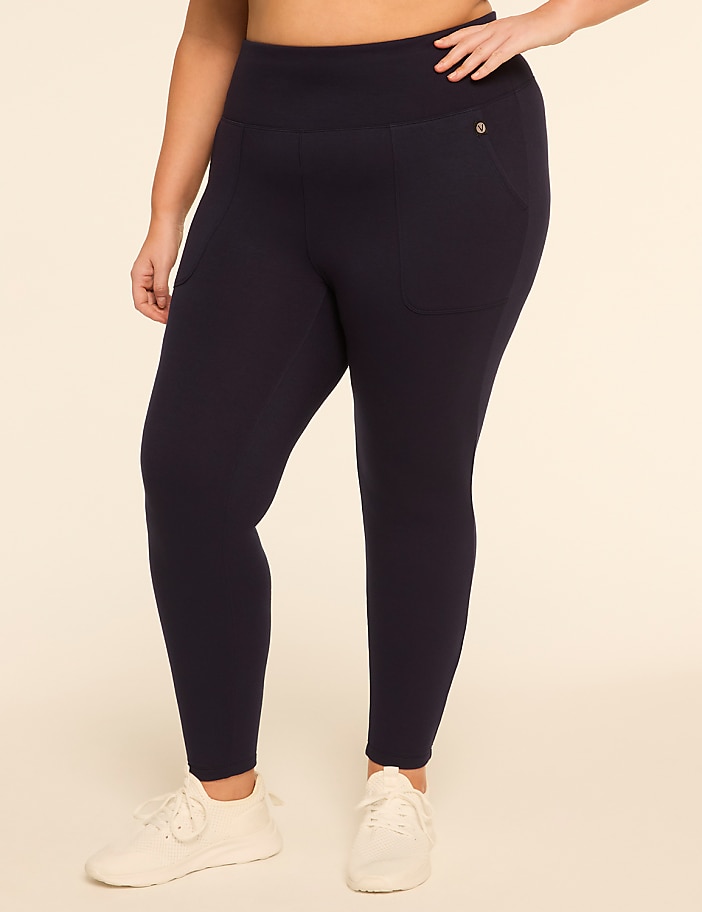 A plus-size woman in navy leggings and white sneakers stands against a plain, light-colored background.